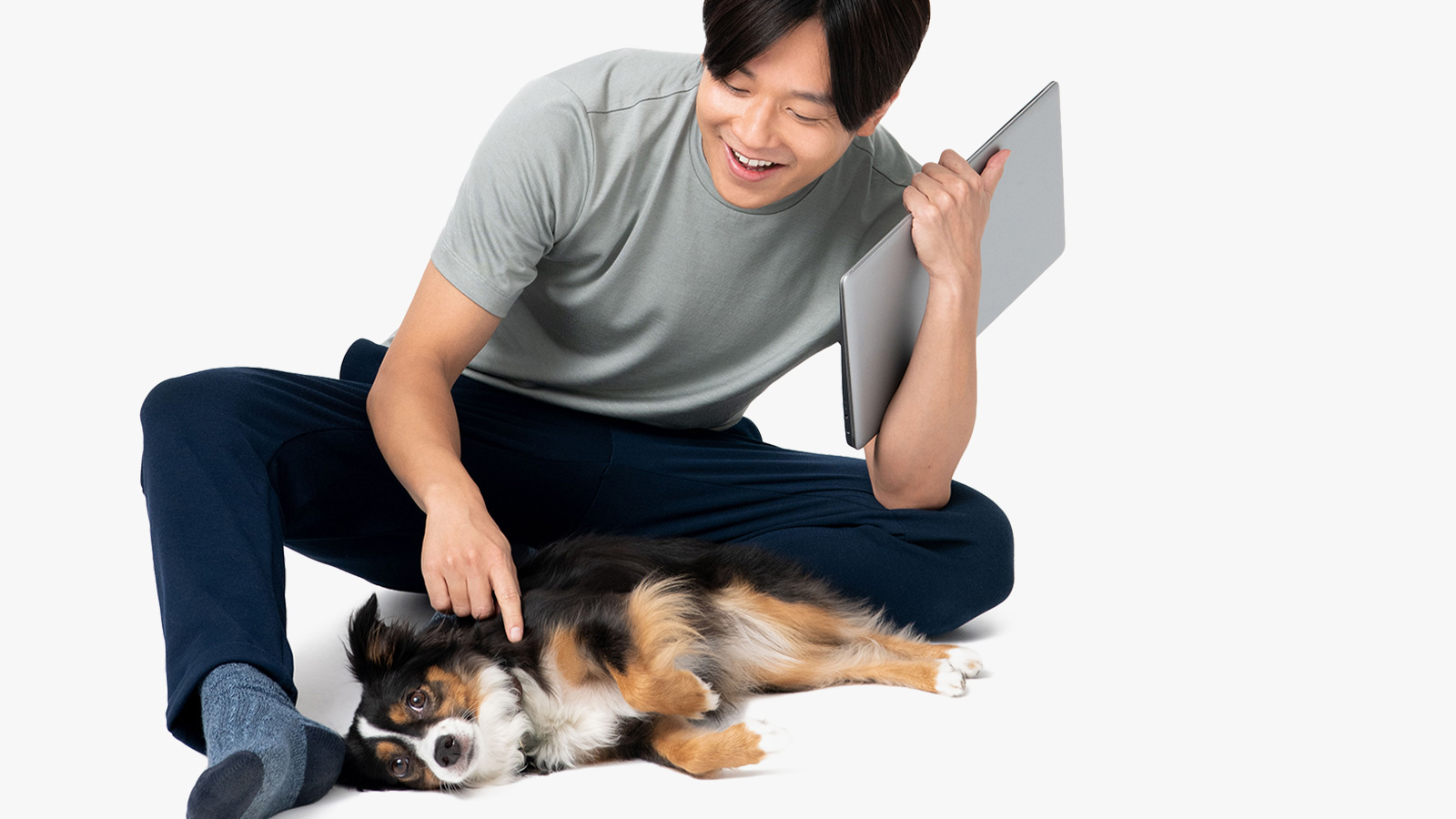 a man petting a dog with their laptop in their left hand